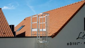 Sunny view of a hotel rooftop with ladder, featuring terracotta tiles and blue sky in Escalles, France.