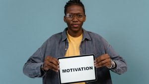 A young African American man holding a tablet displaying the word 'MOTIVATION' against a blue background.